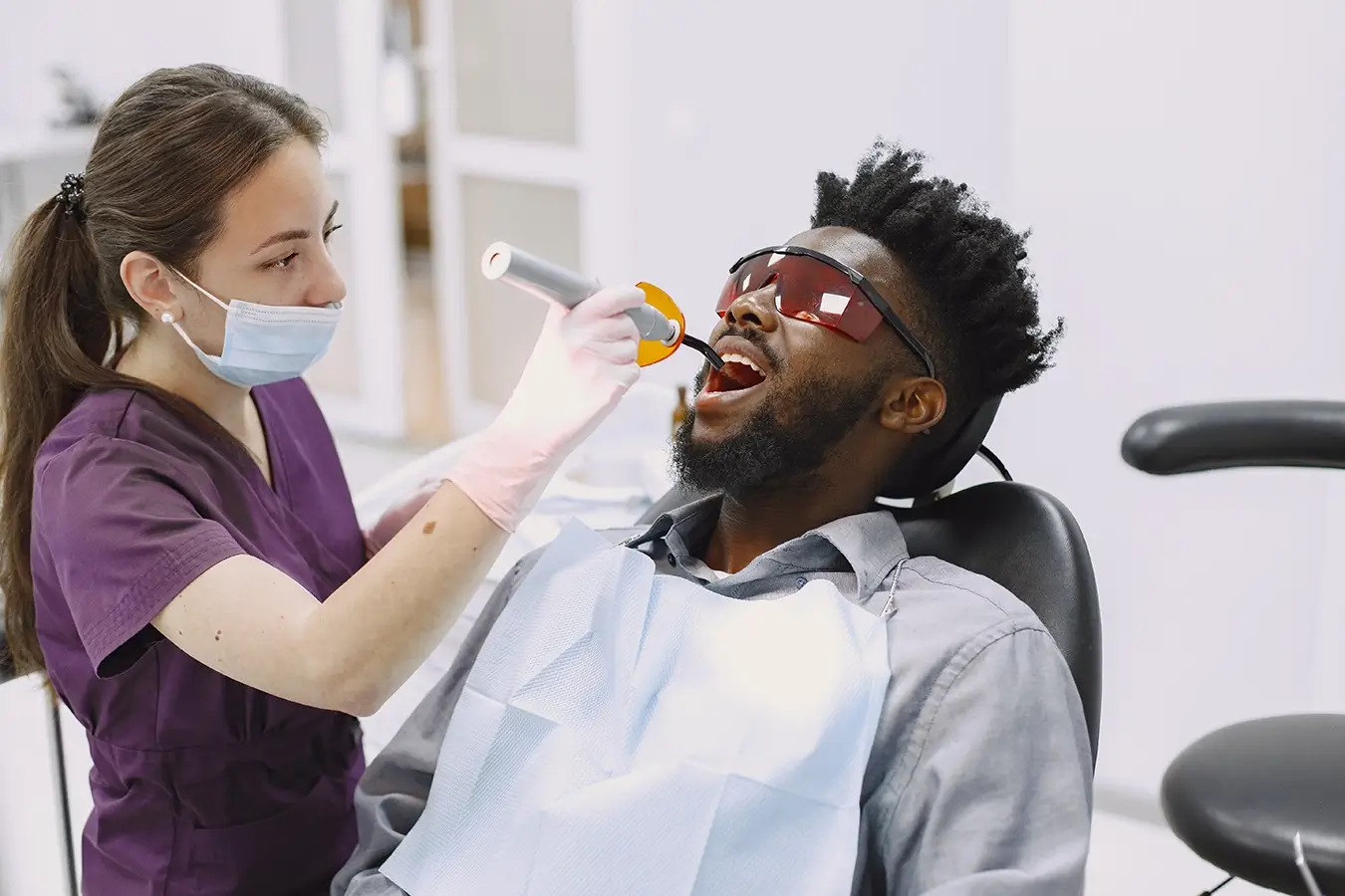 Female dental hygienist wearing gloves and working on a young black male patient