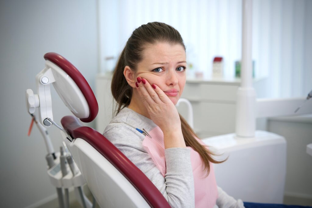 young woman sitting in a modern dental office, suffering from severe tooth pain