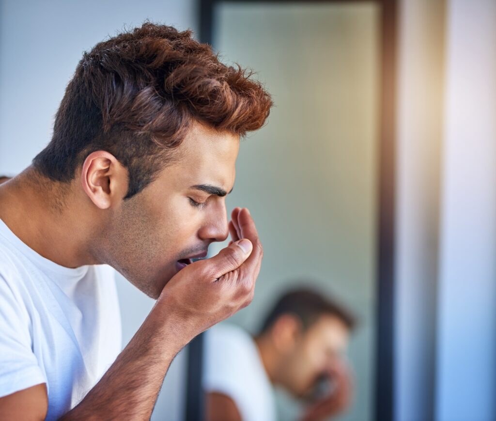 man blowing into his hand checking for bad breath