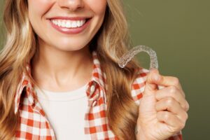 young woman smiling, holding up her clear aligners