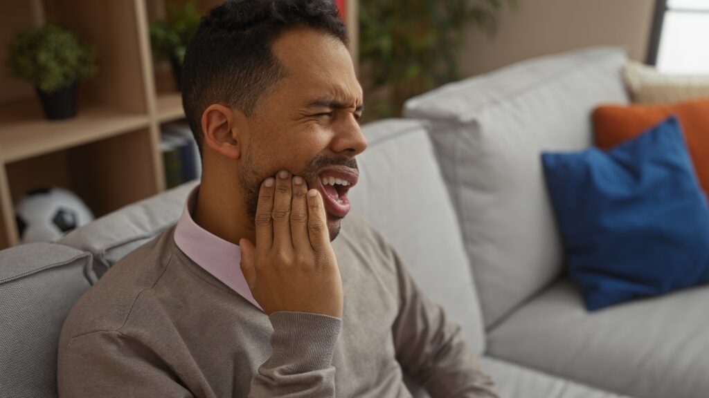 young man sitting on his couch holding his jaw bruxism and jaw pain