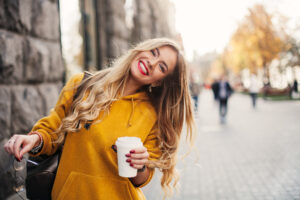 smiling young woman in a yellow sweater, showing off her bright white teeth